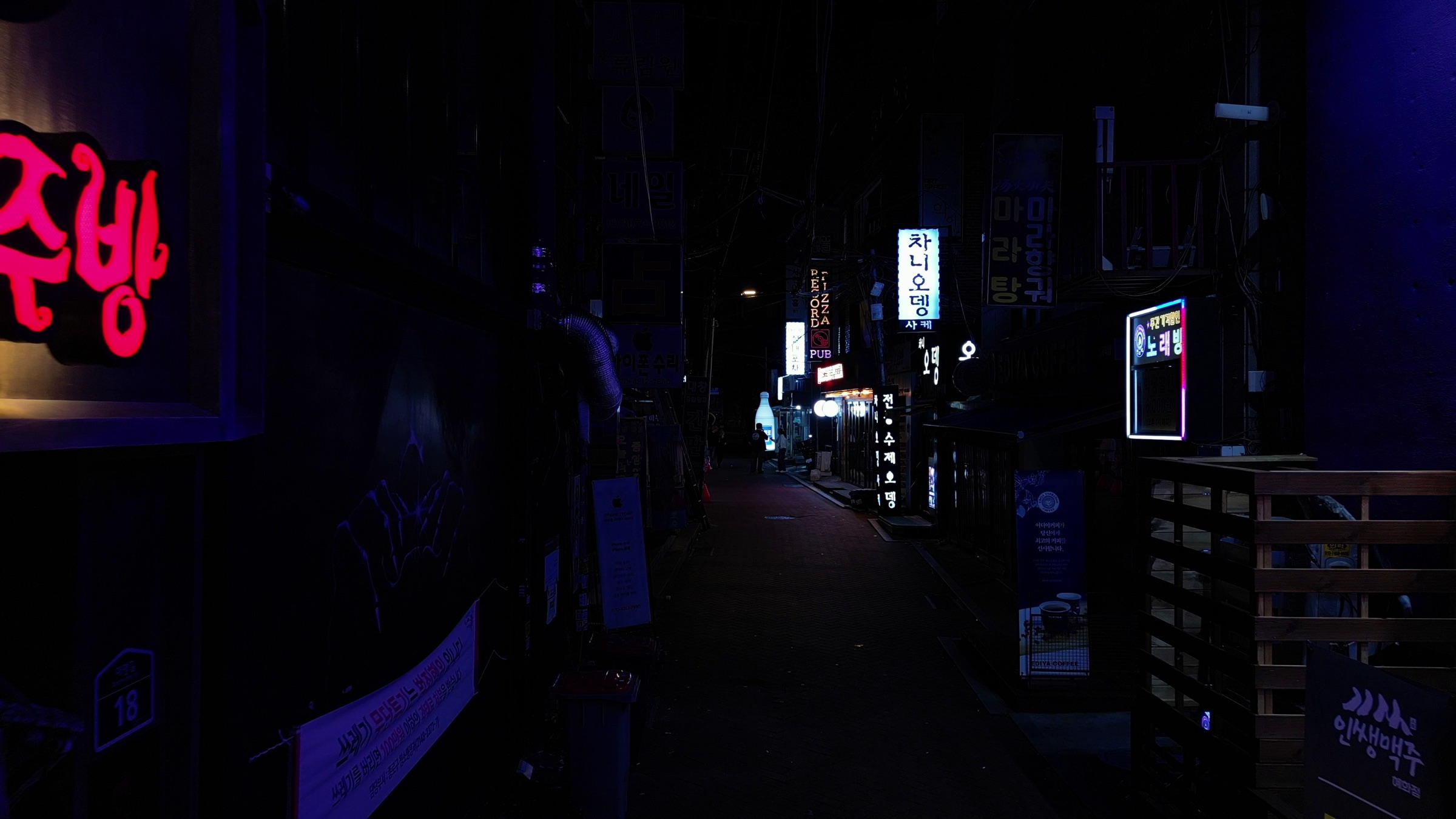 Video still of a dark narrow alley at night lined with illuminated Korean neon signs and shop lights