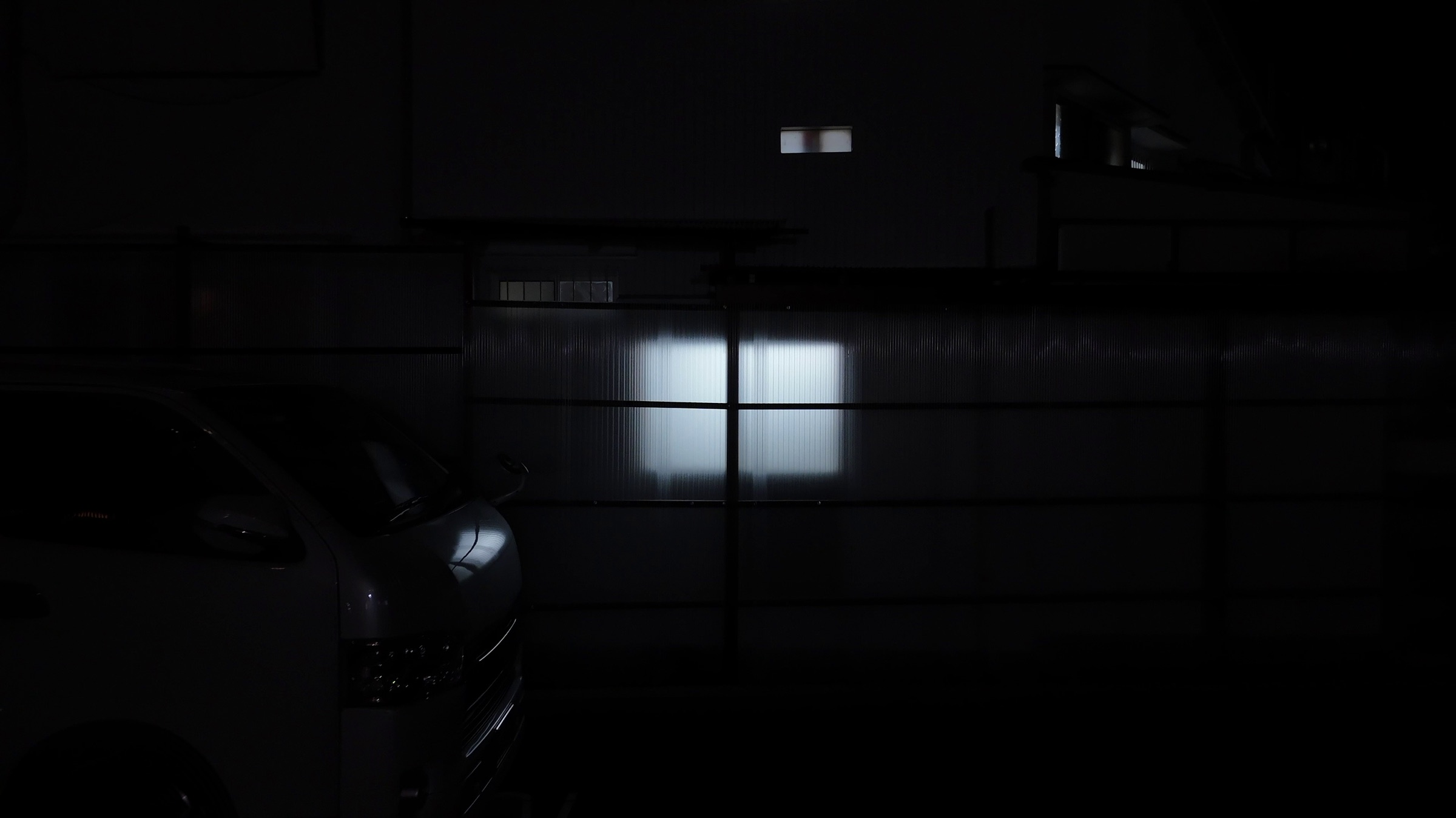 Video still of a dark garage interior with a car silhouette and a backlit corrugated panel wall