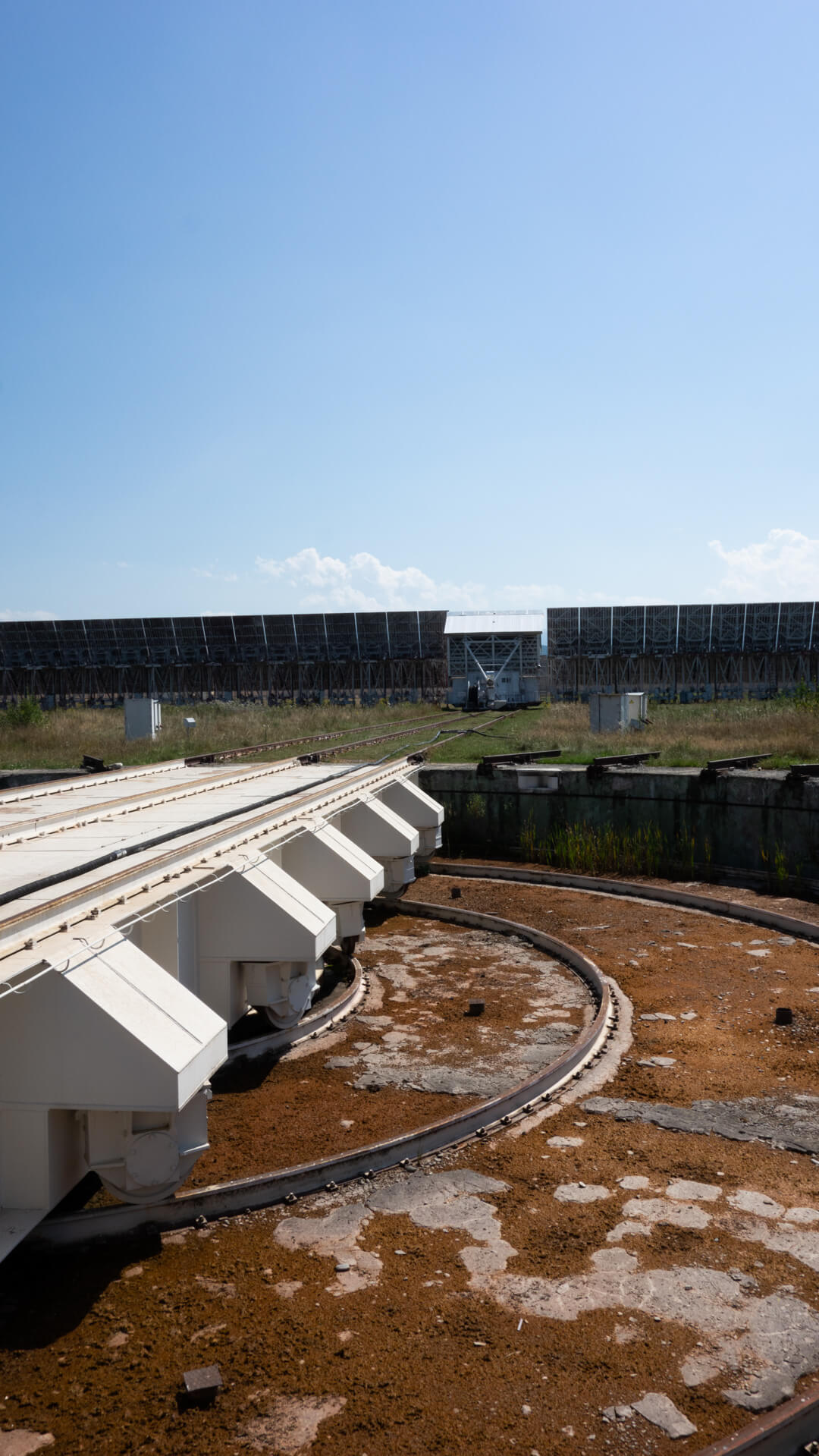 Elevated view of the RATAN-600 radio telescope's curved rail track and antenna panel segments, with the long reflector wall in the background under a clear sky